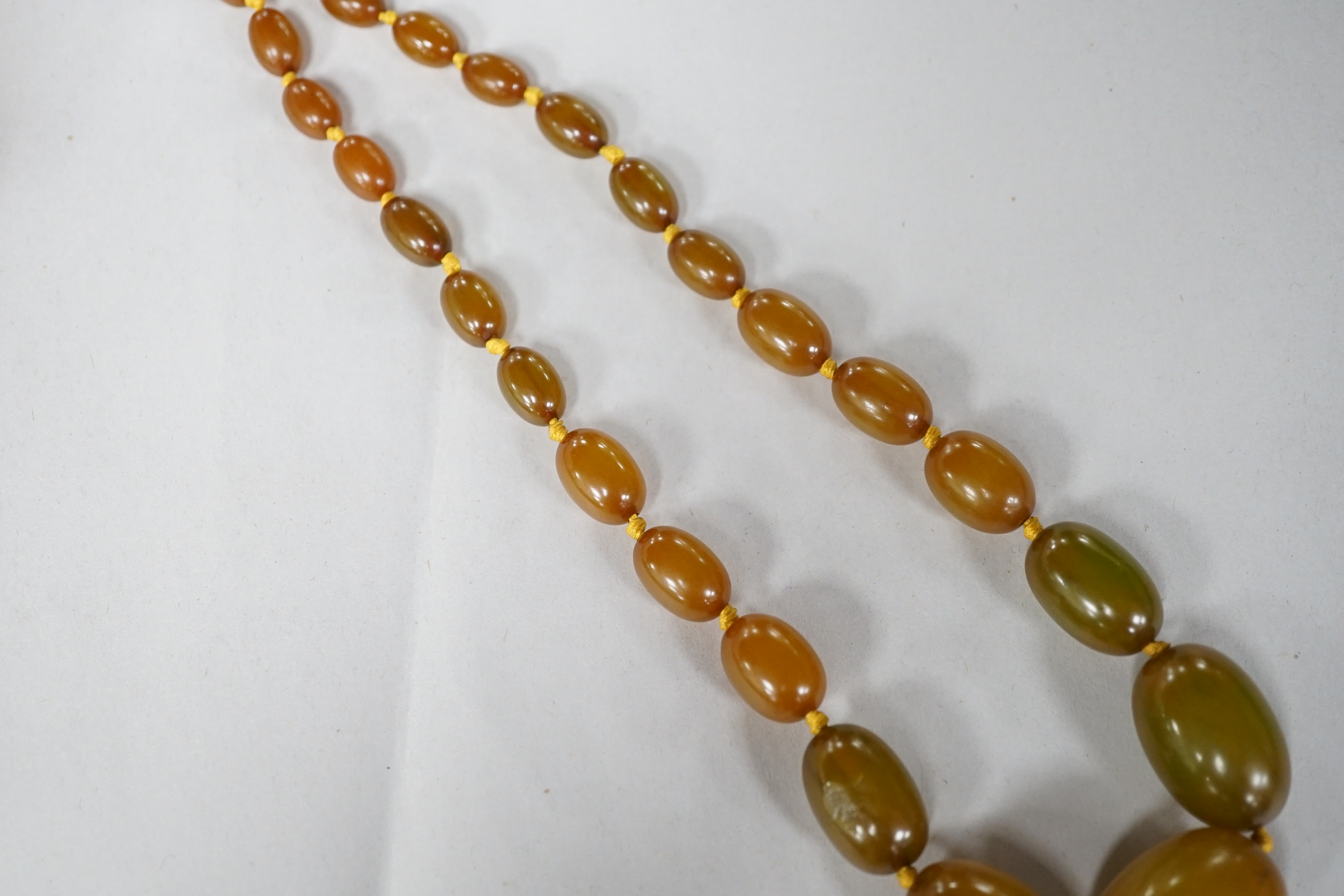 A small single strand graduated oval amber bead necklace, 40cm, gross weight 13 grams, together with a single strand graduated simulated green amber oval bead necklace, 54cm, gross weight 55 grams. Condition - poor to fa